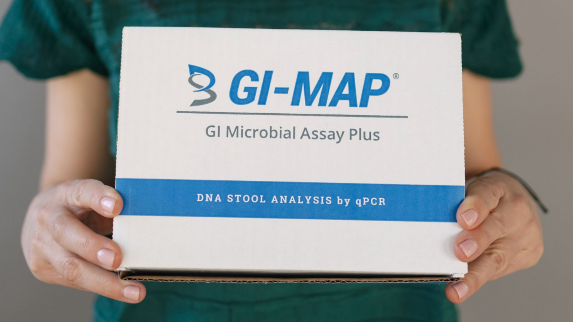 Hands holding a GI-MAP GI Microbial Assay Plus DNA stool analysis test kit box